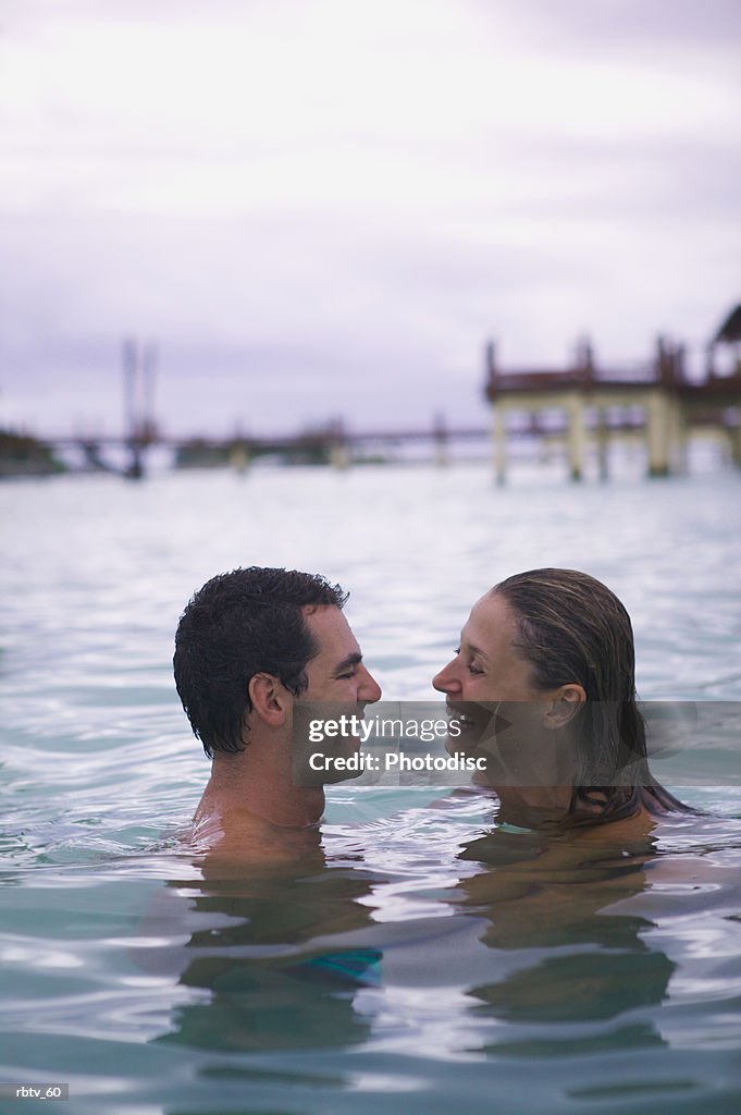 A caucasian couple swim together at a beach while vacationing in the tropics