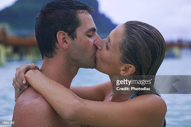 a caucasian couple hug and kiss each other while swimming at a tropical beach - society islands stock pictures, royalty-free photos & images