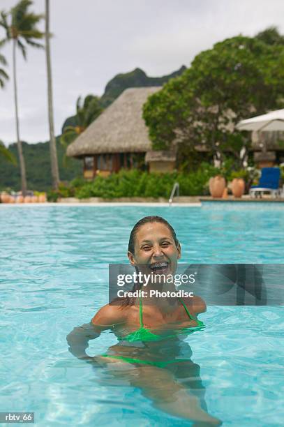 a caucasian woman in a green bikini laughs and smiles in a pool at a tropical resort - gesellschaftsinseln stock-fotos und bilder