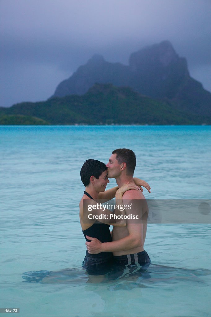 A caucasian couple embrace in the shallow water at a tropical beach