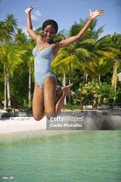 an attractive african american woman in a swimsuit jumps up playfully at the beach - windward islands stockfoto's en -beelden
