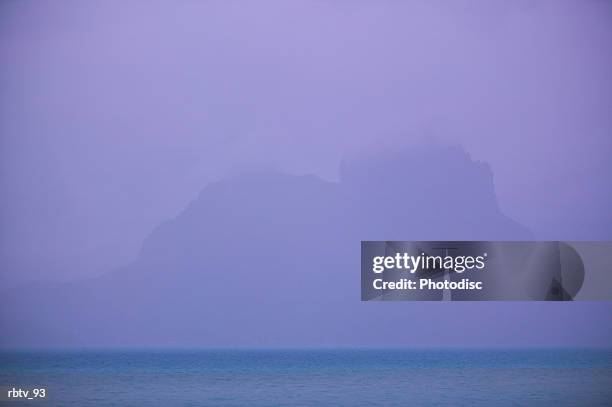 landscape photograph of an island mountain seen through the ocean mist - gesellschaftsinseln stock-fotos und bilder