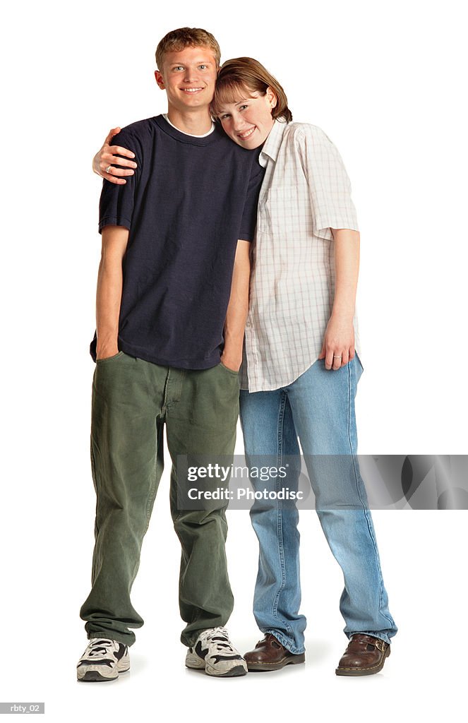 Teenage caucasian girl and boy standing close with her arm around him and her head on his shoulder as they smile at the camera
