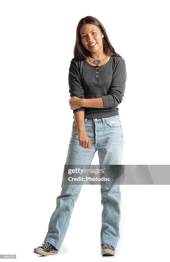 Beautiful young native american woman dressed in gray shirt and blue jeans holds her arm while smiling into the camera
