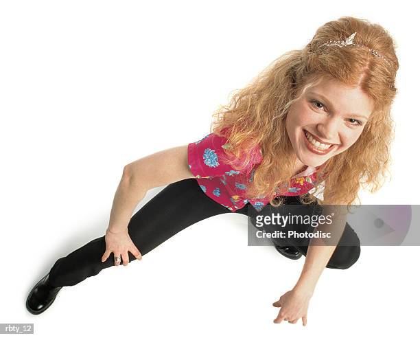 young caucasian woman with red hair dressed in a flower shirt and black pants with a headband leans to her left while looking up at the camera with a big smile and blue eyes - finger waves stockfoto's en -beelden