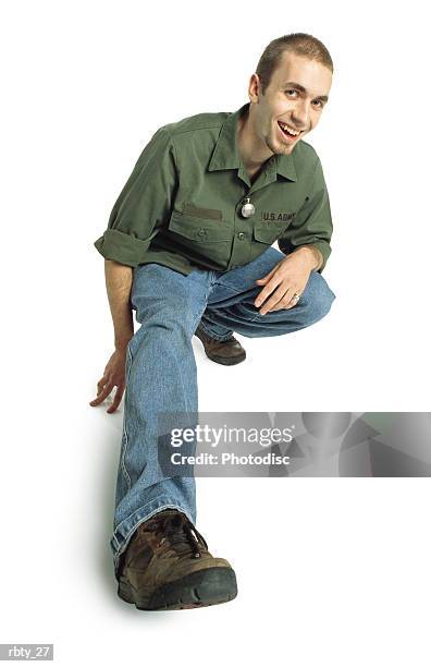 college-age young man with a small beard and short hair wearing a green army shirt blue jeans and brown shoes squats down and sticks one foot out towards the camera and smiles - crew cut stock pictures, royalty-free photos & images