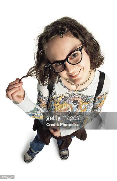 funny teenage girl wearing funky glasses blue jeans a shirt with a dragon painted on it and a sweatshirt around her waist pulls on a lock of her curly hair as she smiles up into the camera - curly stock pictures, royalty-free photos & images