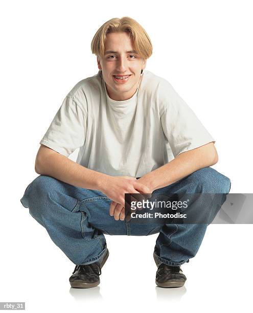 teenage boy with longer blonde hair and braces wearing a white t-shirt blue jeans and black soccer shoes squats down and smiles into the camera - white shirt ストックフォトと画像