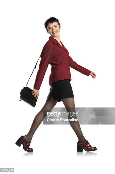 beautiful woman with short dark hair wearing a black mini skirt maroon blazer black nylons red high heeled shoes and purse struts in front of the camera holding her purse and smiling - maroon - fotografias e filmes do acervo