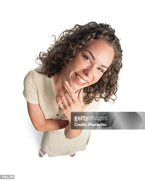 cute young woman with curly brown hair wearing a cream top and skirt looks up to the camera happily as she brings her hand up to her chin - curly stock pictures, royalty-free photos & images