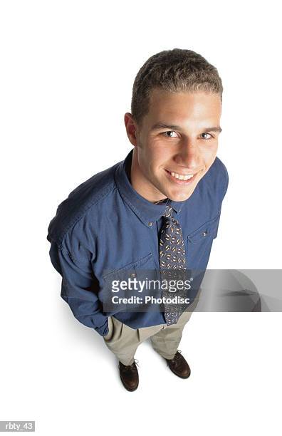 handsome young man with short curly blonde hair and blue eyes wearing a blue shirt and tie tan pants and brown shoes looks up to the camera and smiles - curly stock pictures, royalty-free photos & images