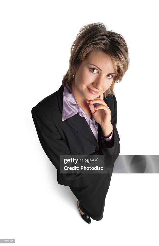 Beautiful business woman with short brown hair wearing a purple shirt under a dark suit looks up at the camera and poses with one hand to her chin and smiles