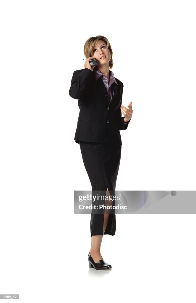 Beautiful business woman with short brown hair wearing a purple silk shirt under a dark dress suit and skirt and black shoes talks into a cellular phone as she looks off into the distance