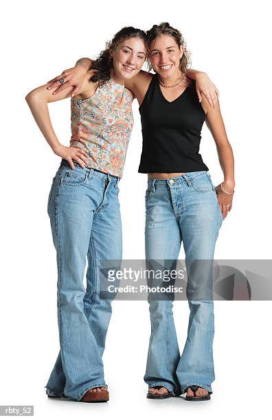 two teenage girls with curly brown hair stand with their arms around each others shoulders wearing tank tops and blue jeans they smile at the camera - smile stockfoto's en -beelden