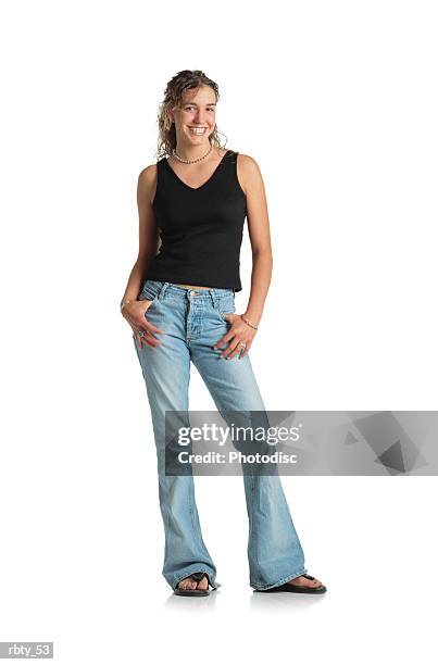 young teenage female with brown long curly permed hair pulled back halfway wearing a black tank top blue jeans and thongs looks into the camera and smiles - girl in tank top stock-fotos und bilder