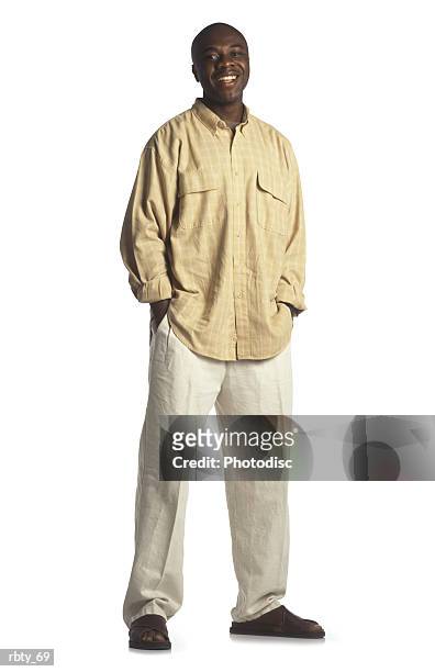 african american college student with no hair wearing a yellow linen shirt and cream linen pants with brown sandals stands with his hands in his pockets and his feet apart as he smiles into the camera - no stock pictures, royalty-free photos & images