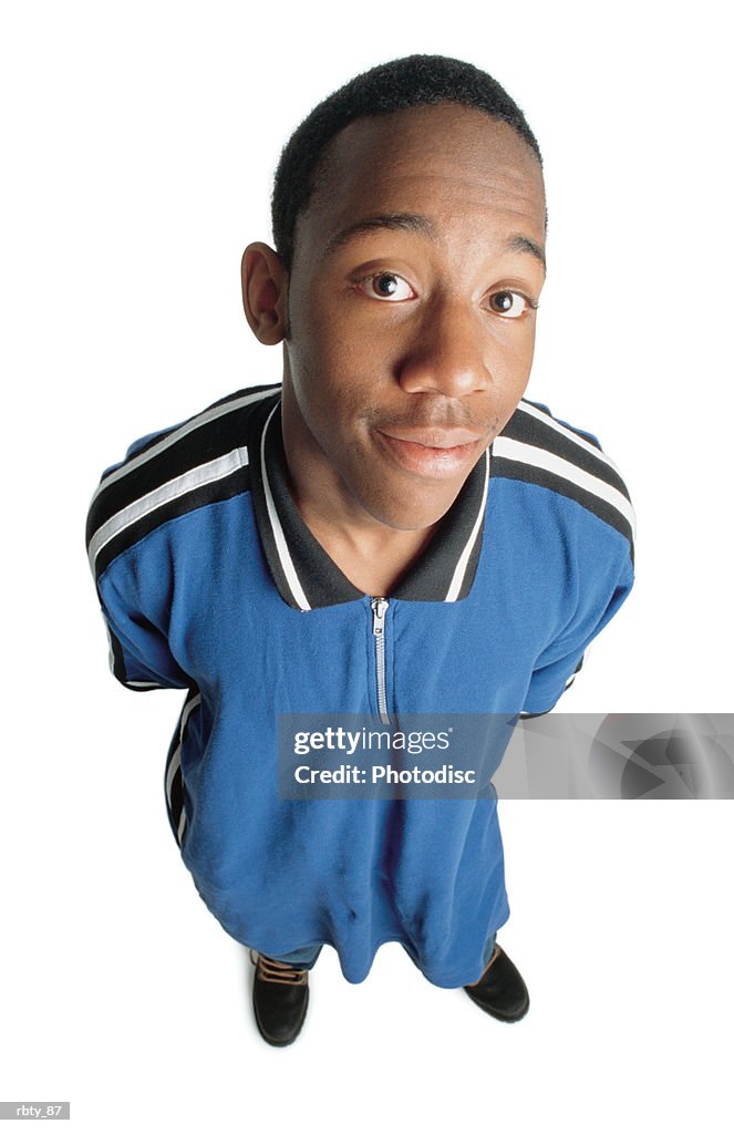 An african-american man with black hair wearing black work boots and a blue shirt with his hands behind his back looks up toward the camera as he smiles