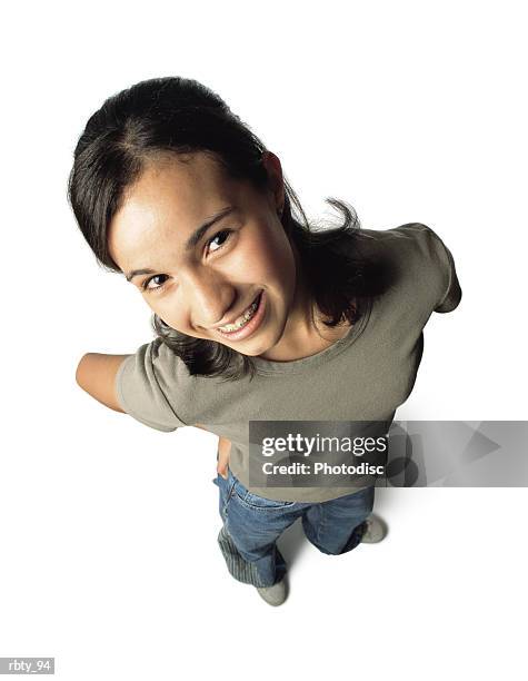black-haired teenage girl wearing blue denim jeans with white shoes and a green shirt puts her hands on her hips as she smiles and looks up toward the camera - white shirt ストックフォトと画像