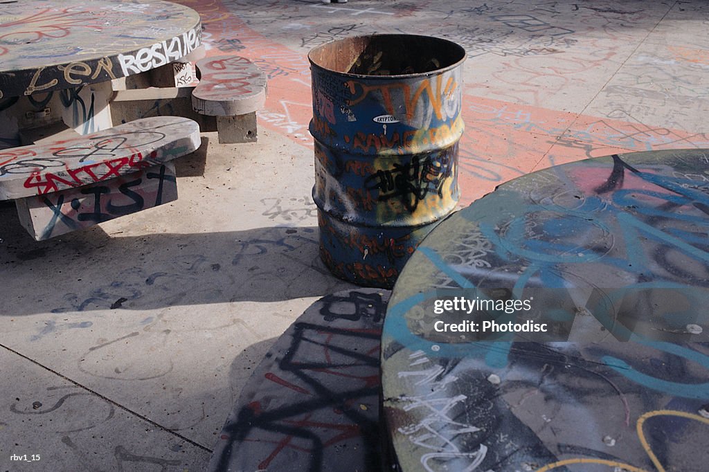 Stone table and benches covered in graffiti with an oil drum for a garbage can