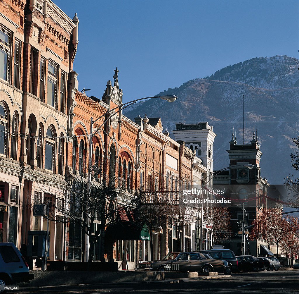 Buildings and cars line the side of a street as the mountains and blue sky rise above them
