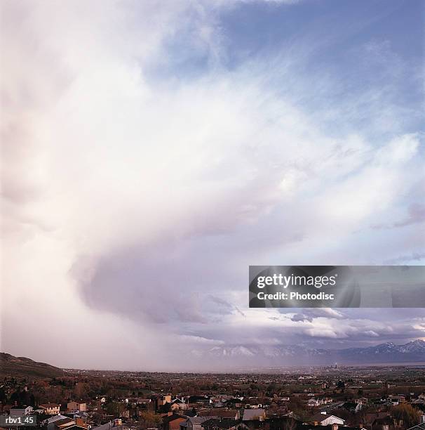 a large white cloud covers a blue sky as houses can be seen below and mountains rise in the background - white cloud mountains stock pictures, royalty-free photos & images