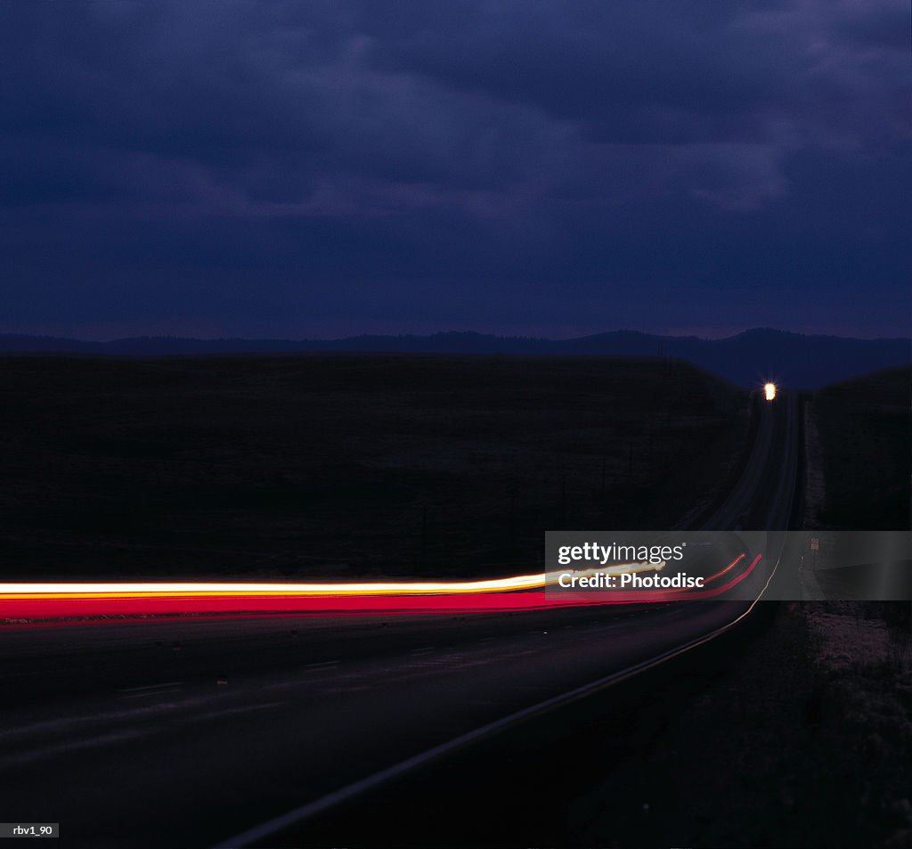 Time lapsed brake lights and headlights travel on a country road to and from a mountains under a dark cloudy night
