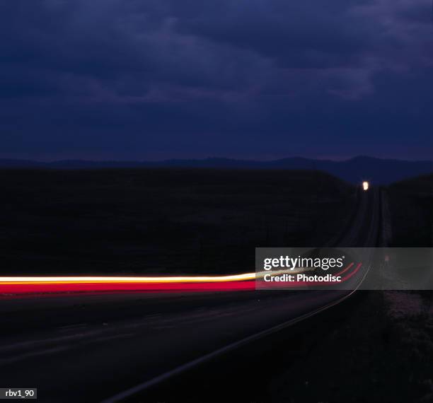 time lapsed brake lights and headlights travel on a country road to and from a mountains under a dark cloudy night - travel​ stock pictures, royalty-free photos & images