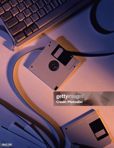 several floppy disks sit on a table next to papers and a computer keyboard as light casts shadows - computer disk stock pictures, royalty-free photos & images