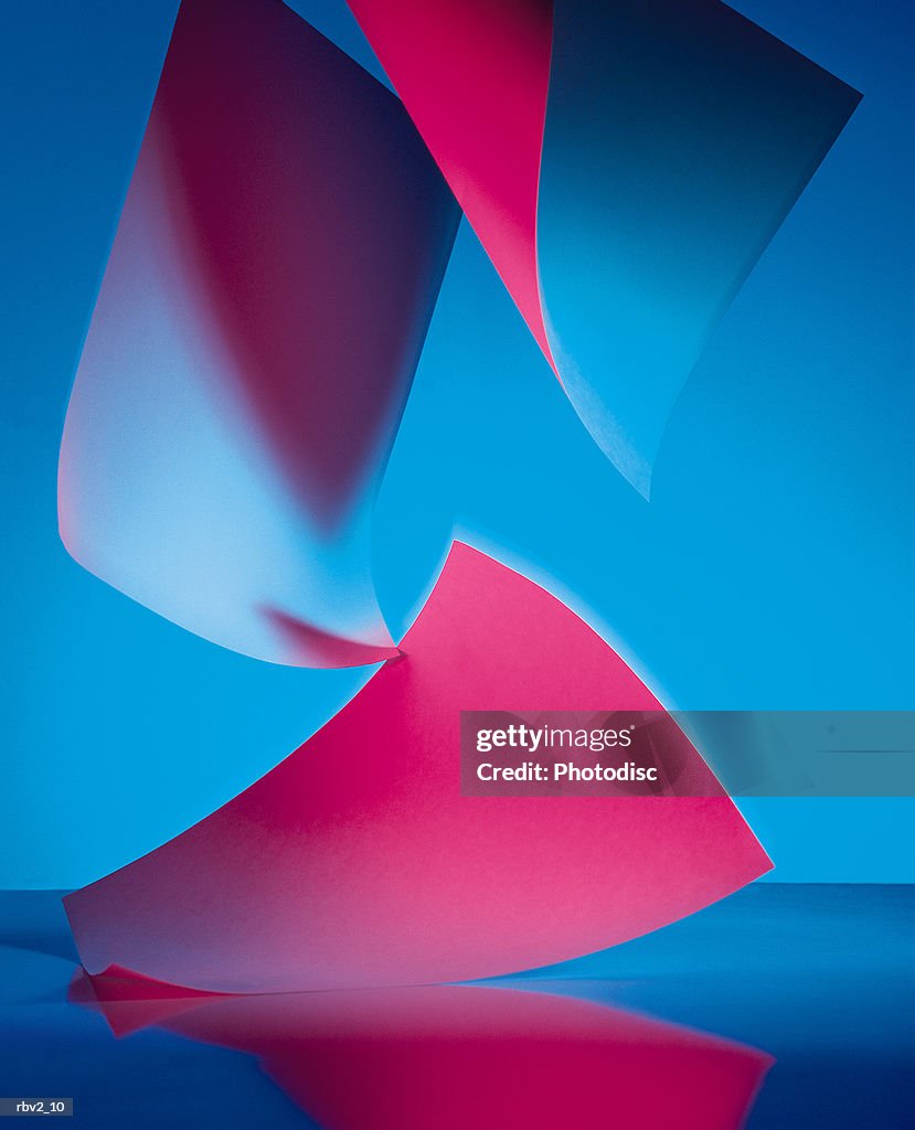 Abstract red and blue colored papers fall to a reflective surface