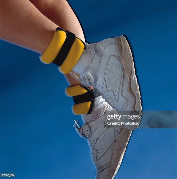 a pair of white shoes and yellow ankle weights rest on legs in front of a blue background - ankle weights stock pictures, royalty-free photos & images