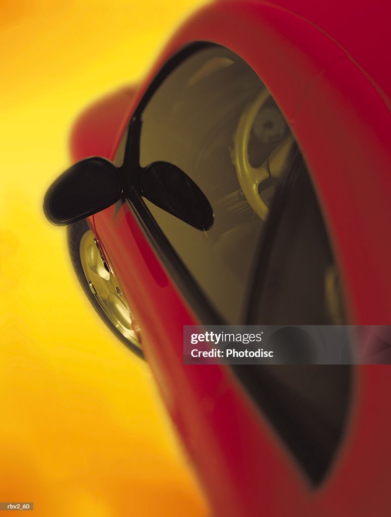 Front and side of a red car with tinted windows rests on a yellow background