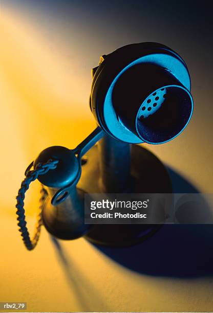 an antique phone with separate receivers for mouth piece and speaker stands in the middle of a yellow light - antique stockfoto's en -beelden