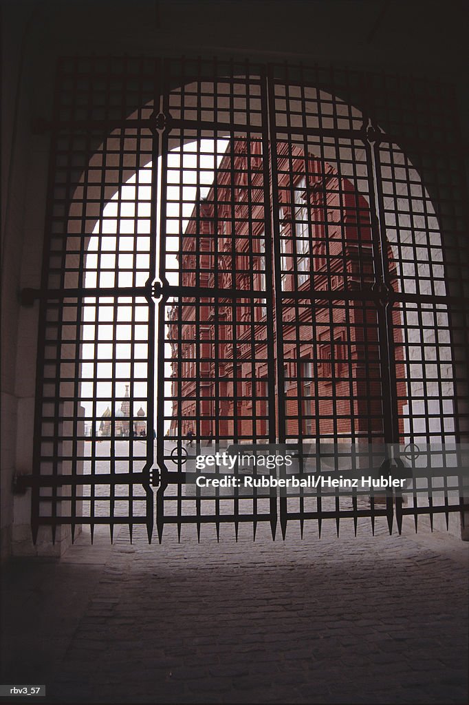 Looking through an arch sealed with a mesh gate looking at a brown building