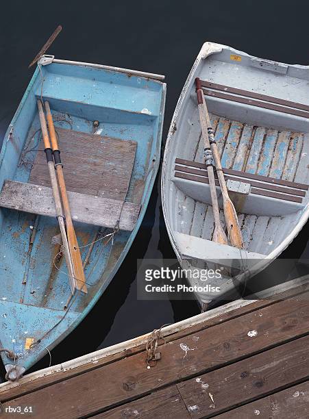 two blue fishing boats with oars float next to each other at the side of a wooden dock - next imagens e fotografias de stock
