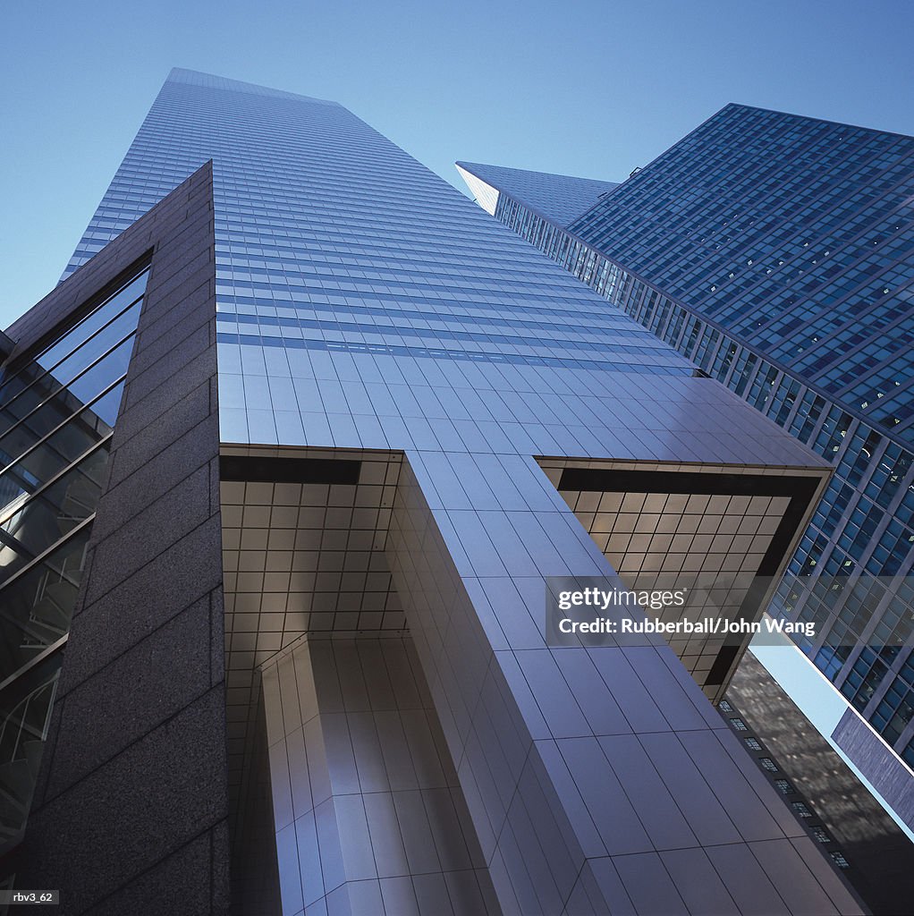 Looking up to see a modern gray building with black windows reaching to a blue sky
