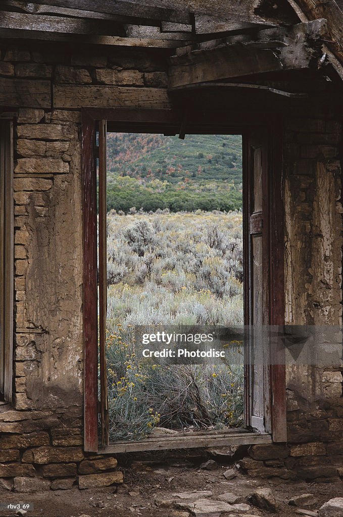 Looking out of an abandoned adobe cabin to see sage brush and dead grass