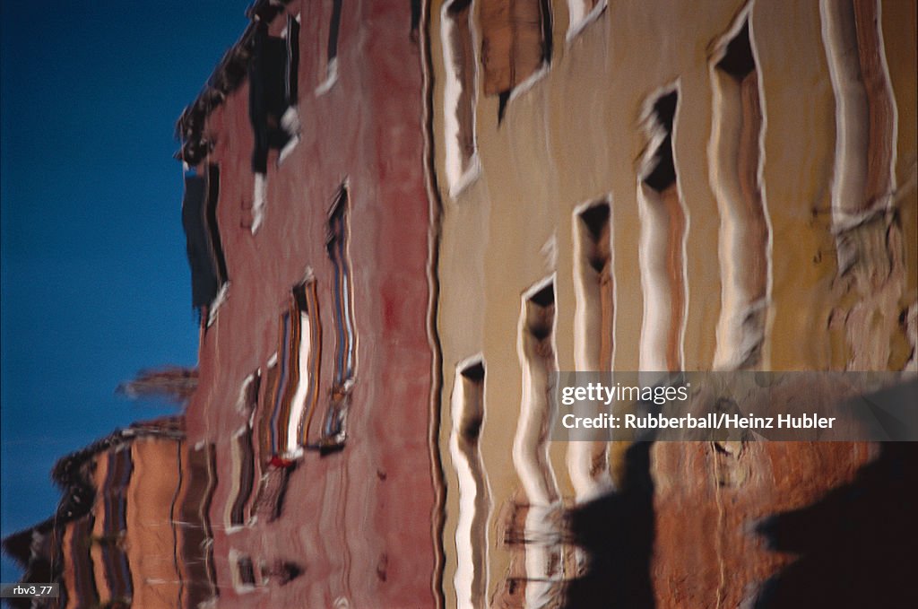 Maroon and beige buildings with white frames can be seen reflected in canal water