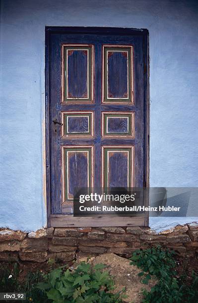 a wooden door stands in a blue stucco wall with green plants below it - door stockfoto's en -beelden