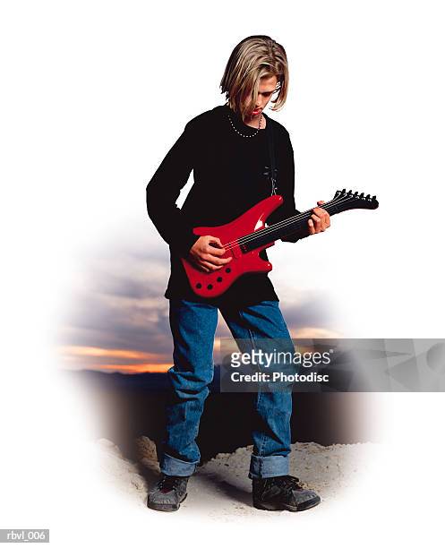 a male caucasian youth with long blond hair wearing a black shirt and blue jeans is standing outside playing an electric guitar - plucking an instrument foto e immagini stock