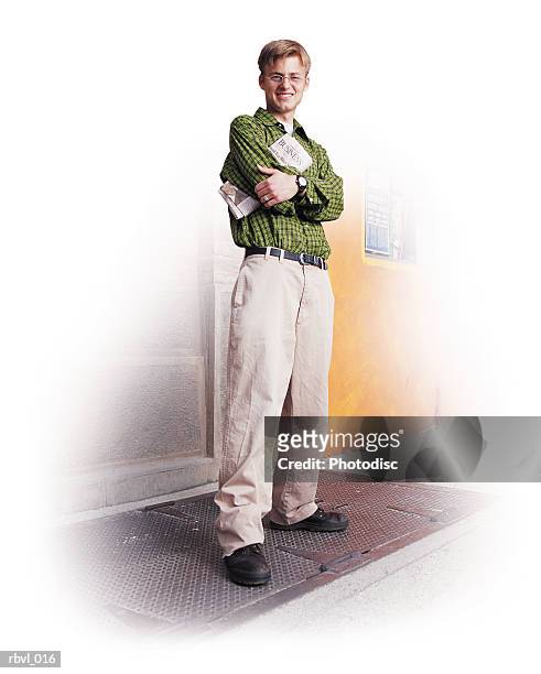 a young caucasian man in a green shirt and tan pants is standing with his arms crossed and smiling at the camera - tan tan stock pictures, royalty-free photos & images