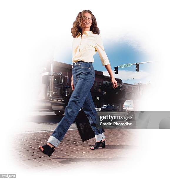 a young hispanic or caucasian woman with curly brown hair in a yellow shirt and blue jeans is walking along a city street - or stock pictures, royalty-free photos & images