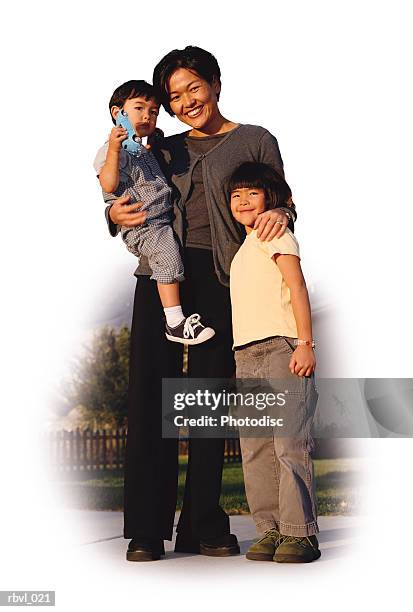 a young asian mother wearing dark pants and blouse is holding her toddler son and has her arm around her little girl as they smile towards the camera - smile imagens e fotografias de stock