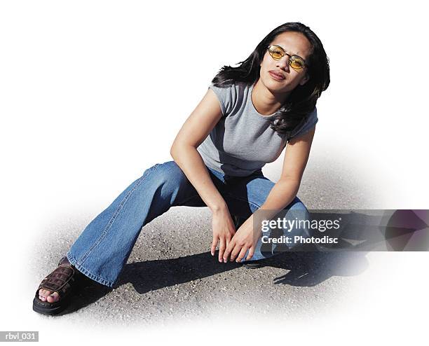 a dark haired young polynesian woman in blue jeans and a gray shirt is crouching down on one knee in a parking lot and looking into the camera - the lot stock-fotos und bilder