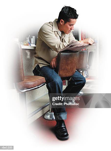 a short haired hispanic man wearing blue jeans and a tan long sleeved shirt is sitting at the counter of a diner reading a newspaper - tan tan stock pictures, royalty-free photos & images