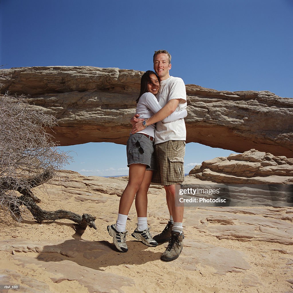 Young man checkered shorts t-shirt hugs young woman in gray shorts white shirt at a natural arch