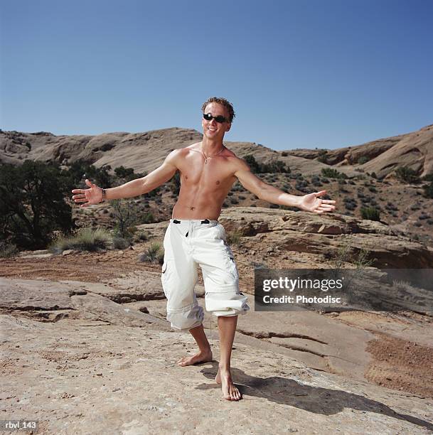 a tan caucasian young man in sunglasses is wearing baggy white pants and no shirt as he stands gesturing with outstretched arms toward the camera - no stock pictures, royalty-free photos & images