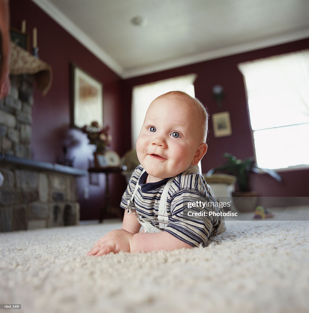 A smiling caucasian baby boy is crawling on a white carpet and smiling at the camera