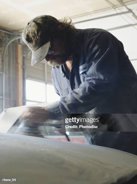 a caucasian man works on a car in a shop - sandblasting stockfoto's en -beelden