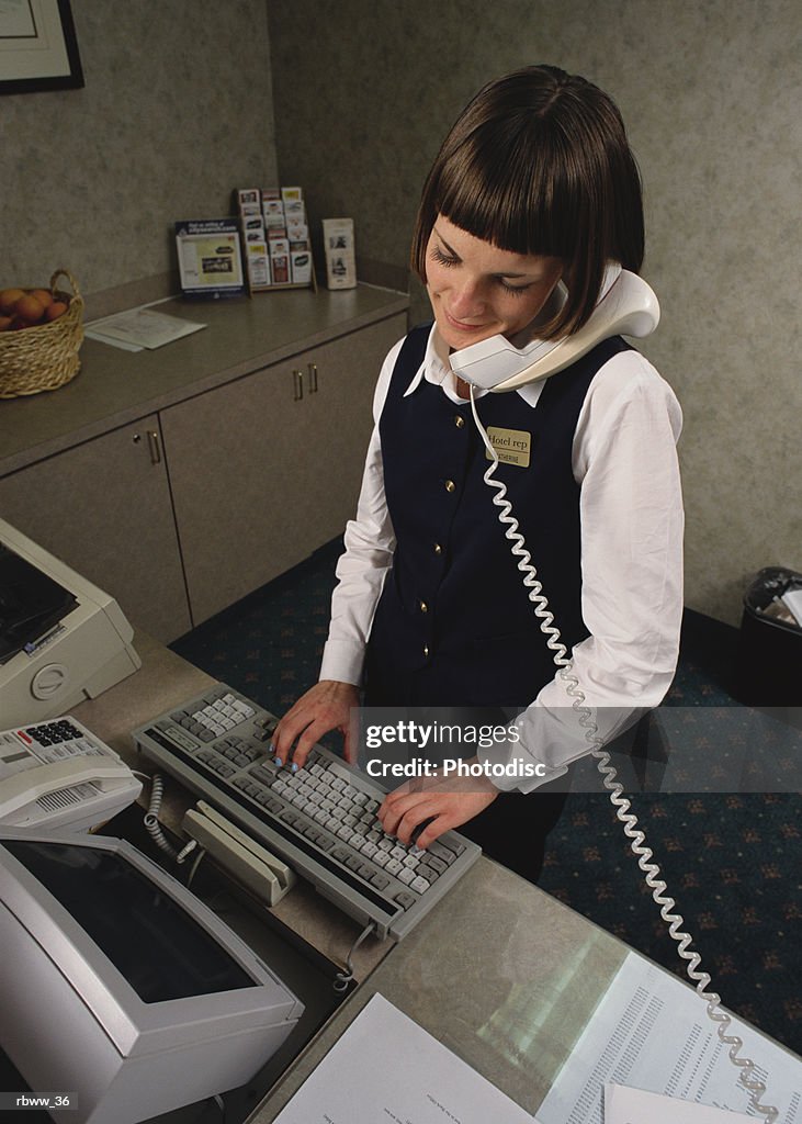 A hotel attendant logs a customer reservation onto a computer while speaking with him over the telephone