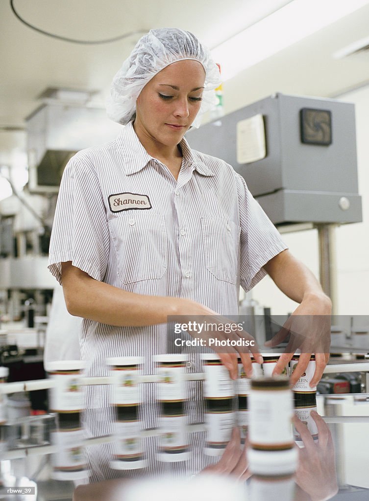 A caucasian woman inspects bottles of pills on a clean-room assembly line